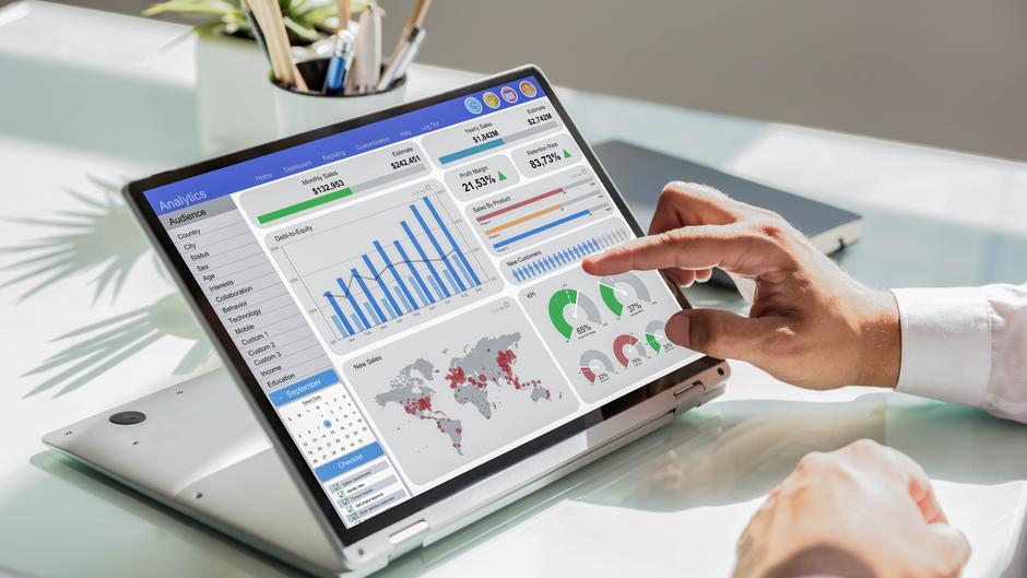 Ein Laptop zeigt ein Analyse-Dashboard mit Diagrammen, Statistiken und einer Weltkarte, während eine Hand darauf tippt.