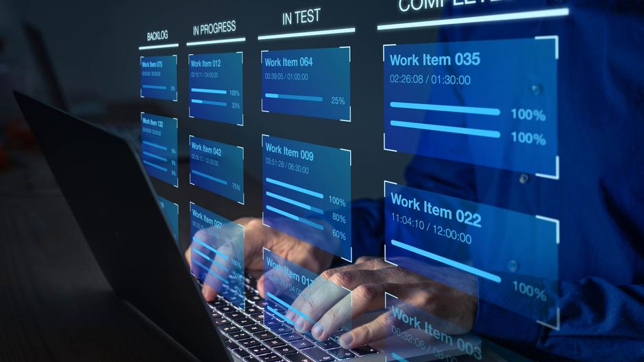 Hände tippen auf einer Laptop-Tastatur, während ein digitales Dashboard mit Fortschrittsanzeigen von Arbeitsaufträgen angezeigt wird.