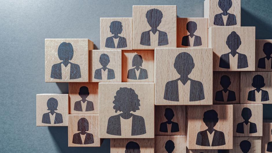 Holzblöcke mit stilisierten Silhouetten von Personen in verschiedenen Posen und Frisuren auf grauem Hintergrund.