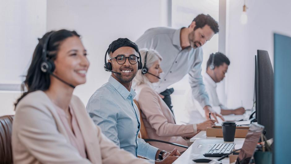 Mitarbeiter in einem modernen Büro mit Headsets, die an Schreibtischen arbeiten und miteinander kommunizieren.