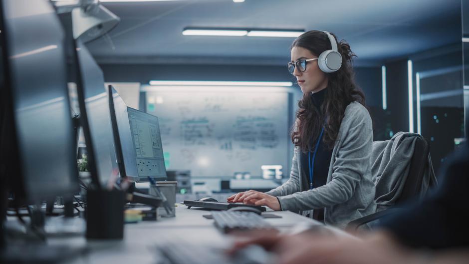 Eine Person mit Kopfhörern arbeitet konzentriert an einem Computer in einem modernen Büro.