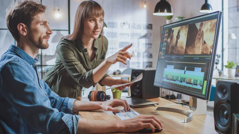 Zwei Personen arbeiten an einem Computer, während sie einen Video-Editing-Prozess besprechen.