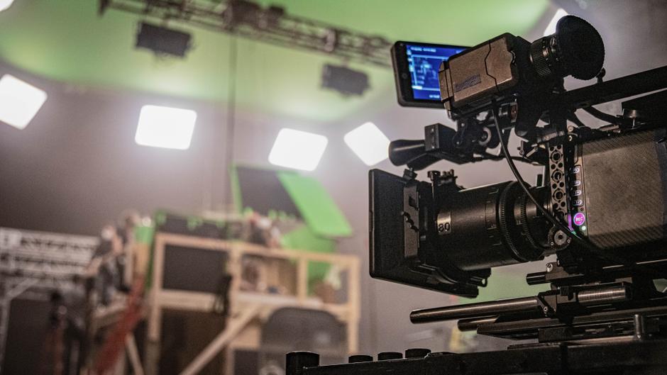 Kamera mit Monitor in einem Studio mit grüner Kulisse und mehreren Scheinwerfern im Hintergrund.