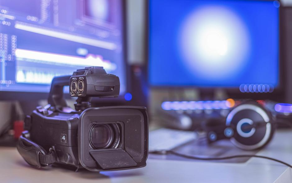 Videokamera im Vordergrund mit zwei Monitoren und Kopfhörern im Hintergrund.