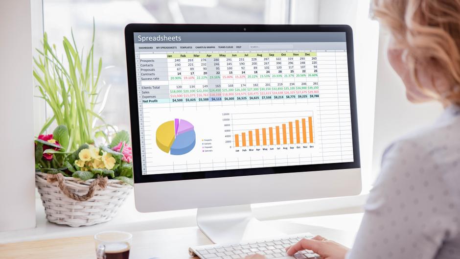 Eine Person sitzt vor einem Computer, auf dem eine Tabelle mit Finanzdaten und Diagrammen angezeigt wird.