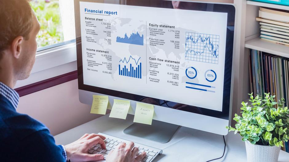 Mann betrachtet einen Computerbildschirm mit einem Finanzbericht und Diagrammen, Post-its sind auf dem Monitor befestigt.