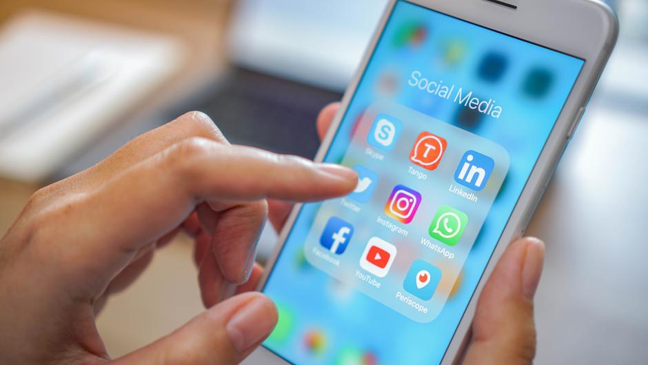 Hand mit Finger, der auf ein Smartphone-Display mit Social-Media-Apps tippt.