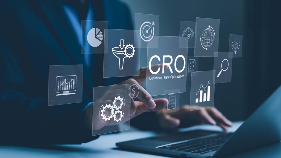 Hand, die auf ein Display mit Symbolen zur Conversion-Rate-Optimierung (CRO) zeigt, vor einem Laptop.