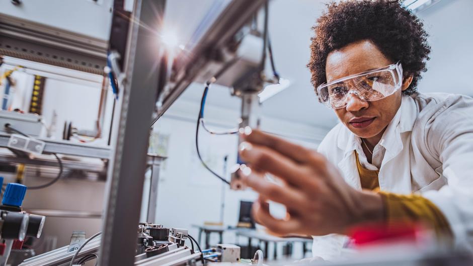 Eine Person in Schutzbrille und Laborkittel arbeitet konzentriert an einer technischen Vorrichtung.