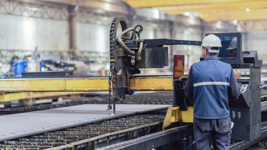 Ein Arbeiter steuert eine CNC-Maschine in einer Fabrikhalle, während Metallplatten bearbeitet werden.