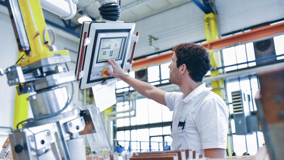 Ein Arbeiter bedient ein digitales Steuerpanel in einer modernen Fabrikhalle.