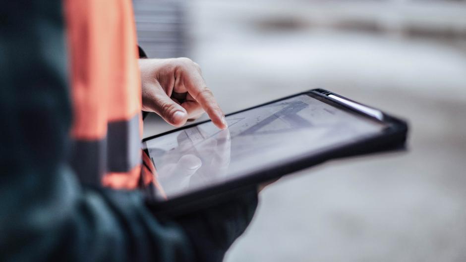 Eine Hand tippt auf ein Tablet, das in einer anderen Hand gehalten wird.