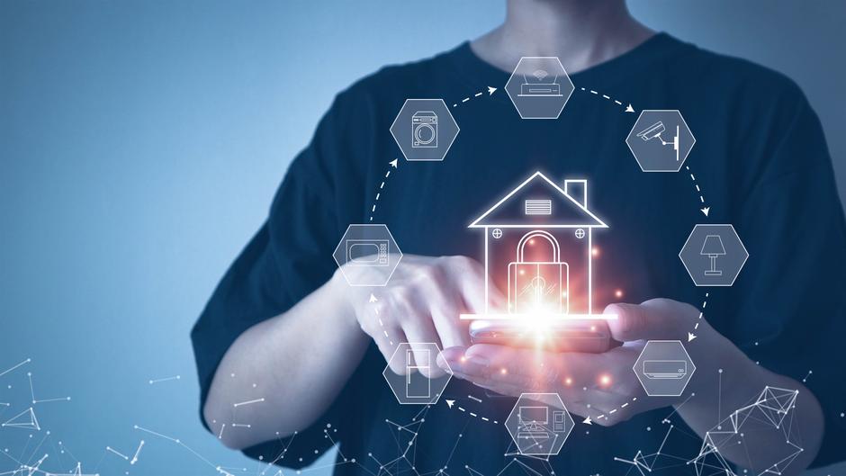Person hält ein Smartphone in der Hand, umgeben von Symbolen für Smart-Home-Geräte und einem Haus-Icon.