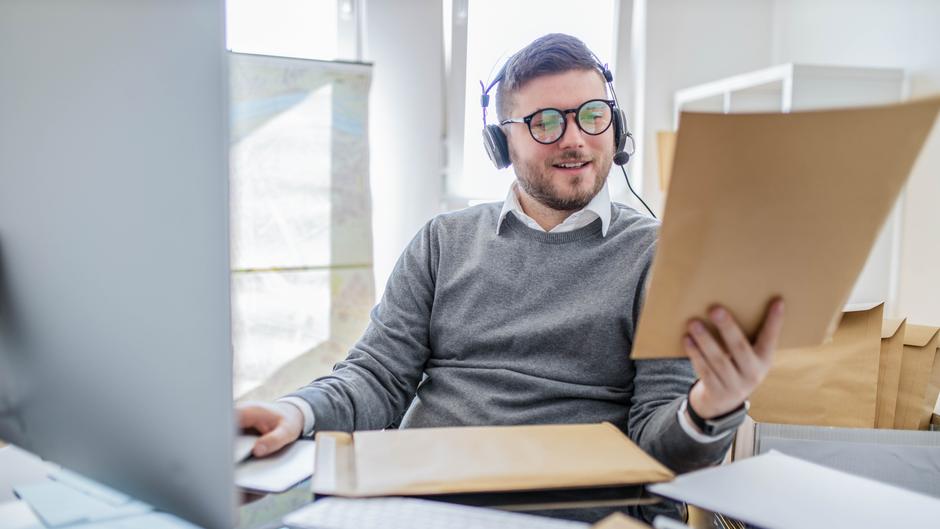 Mann mit Kopfhörern sitzt am Schreibtisch und betrachtet ein Dokument in einem Büro.