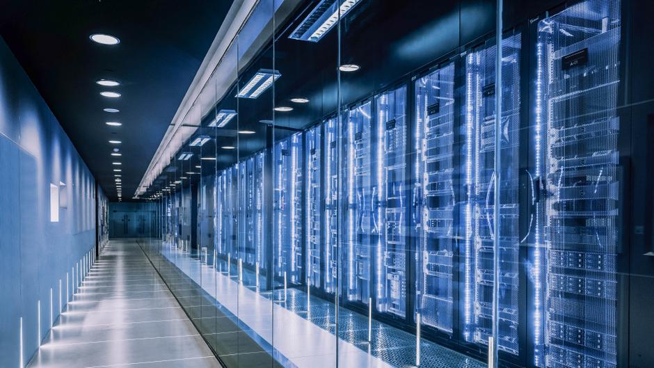 Ein langer, beleuchteter Gang mit Glaswänden und mehreren Server-Racks auf der rechten Seite.