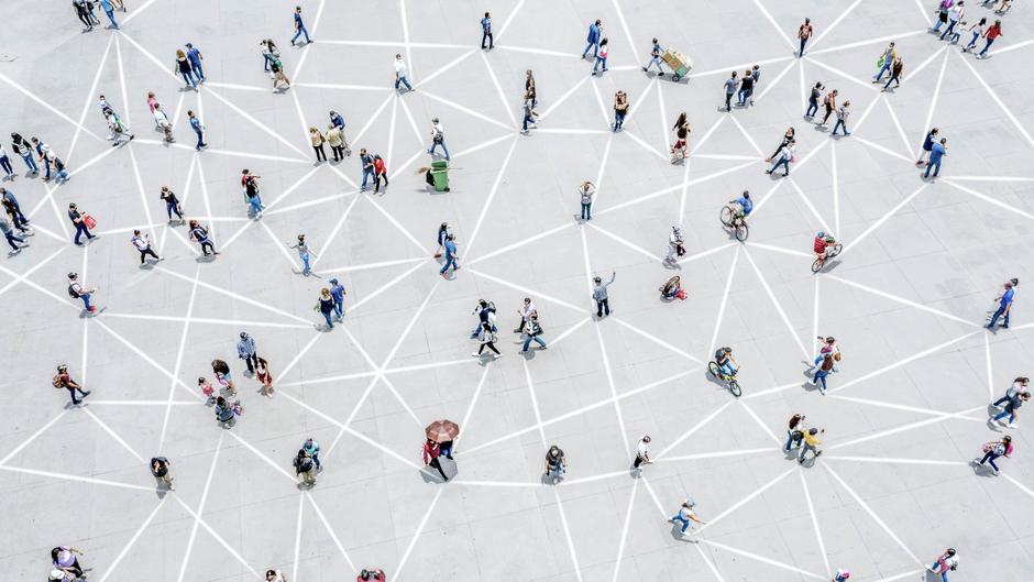 Menschen bewegen sich auf einem Platz, der mit weißen Linien in einem geometrischen Muster markiert ist.