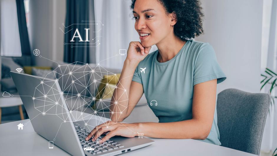 Eine Person mit lockigem Haar sitzt an einem Tisch und arbeitet konzentriert an einem Laptop, umgeben von Symbolen für künstliche Intelligenz.