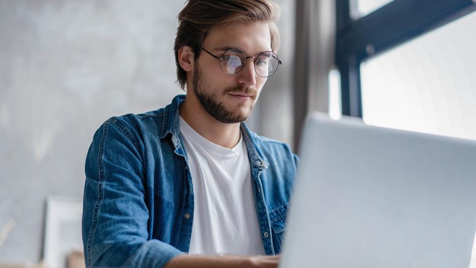 Mann mit Brille sitzt vor einem Laptop und konzentriert sich auf den Bildschirm.