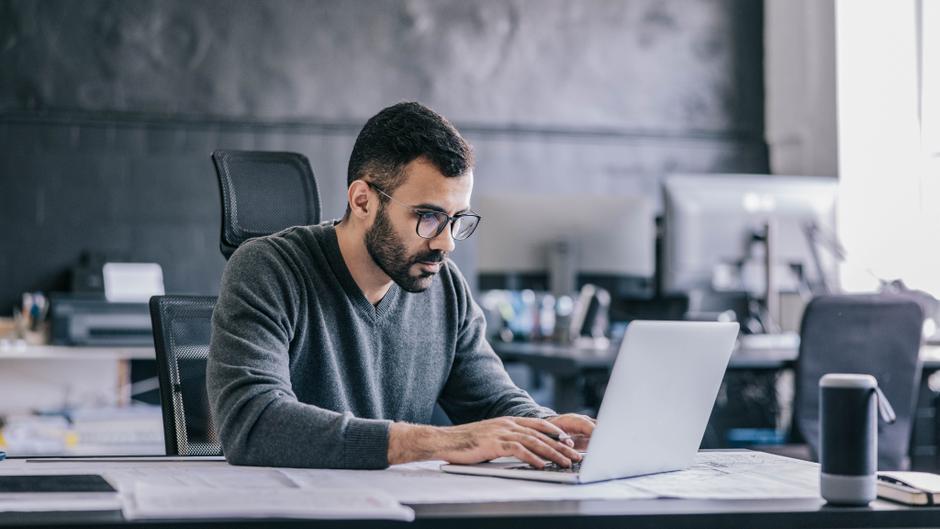 Mann mit Brille arbeitet konzentriert an einem Laptop in einem modernen Büro.