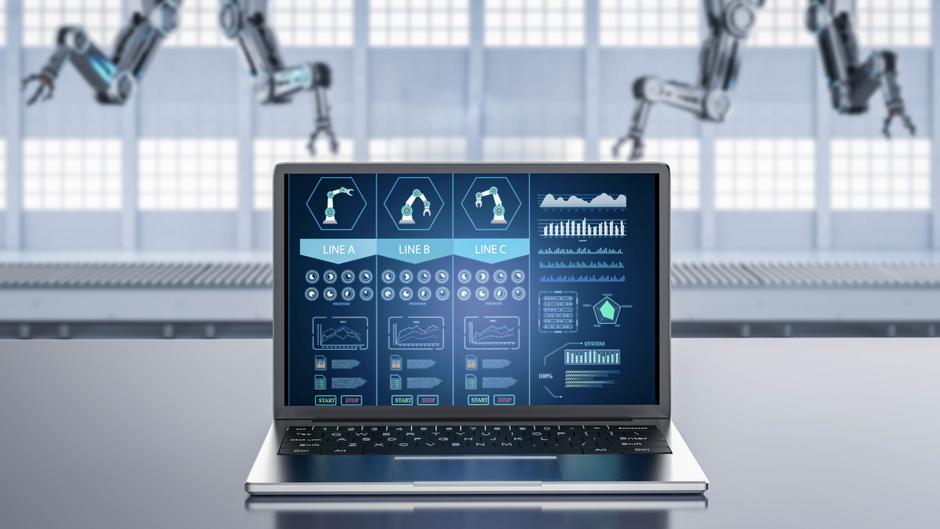 Laptop mit grafischen Benutzeroberflächen für Produktionslinien und Robotersteuerung im Hintergrund.