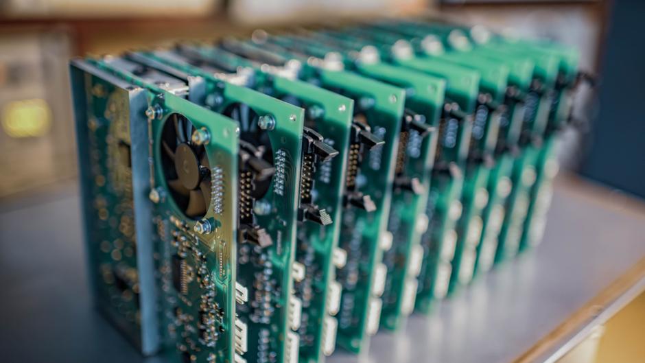 Mehrere grüne Leiterplatten stehen in einer Reihe, einige mit Lüftern und elektronischen Bauteilen.