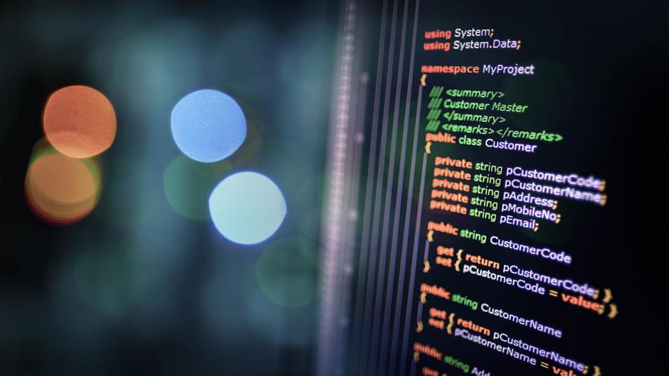Blick auf einen Bildschirm mit Codezeilen in verschiedenen Farben und unscharfen Lichtern im Hintergrund.