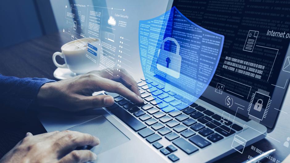 Hände tippen auf einer Laptop-Tastatur, umgeben von digitalen Sicherheits- und Datensymbolen, mit einer Tasse Kaffee im Hintergrund.