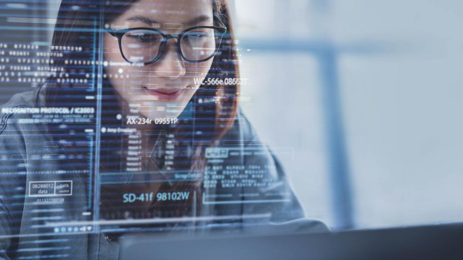 Eine Person mit Brille arbeitet am Laptop, während digitale Daten und Codes im Vordergrund angezeigt werden.