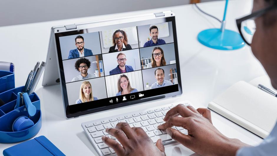 Person tippt auf einer Tastatur, während sie an einem Videoanruf mit mehreren Teilnehmern auf einem Laptop teilnimmt.