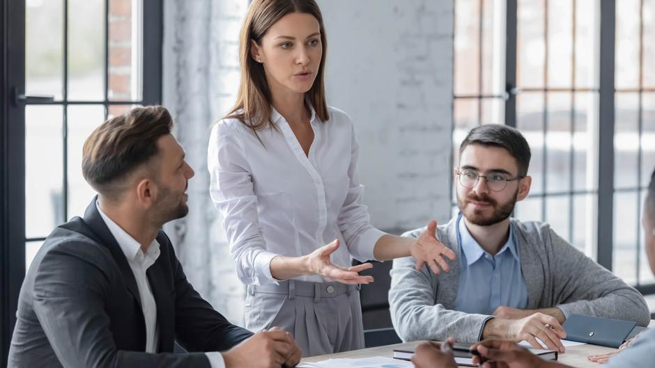 Eine Frau erklärt etwas in einem Meeting, während drei Männer aufmerksam zuhören.